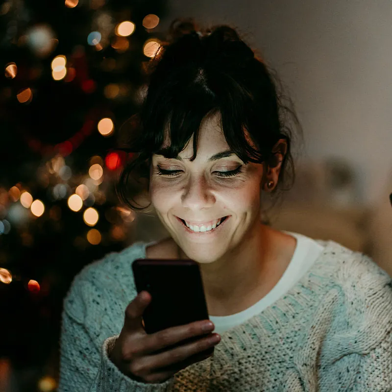 woman looking at phone while christmas tree in a back